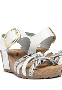 Witte platform sandalen met een kurken zool, voorzien van kruislings lopende zilveren en witte bandjes, een gouden gespsluiting en een soepel leren textuur.