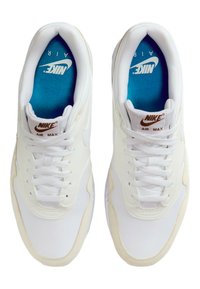Vita Nike Air Max-sneakers med ovandel av mesh och läder, med en ljusbrun logotyp, vita snören och en blå innerfoder.