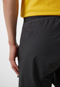 Schwarze Sportshorts mit einem strukturierten Muster am Bund. Sie verfügen über einen elastischen Bund und einen glatten Stoff, der bis zu den Beinen reicht.