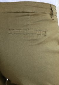 Pantalones verde oliva hechos de una tela suave, que cuentan con un solo bolsillo trasero, con un corte recto y detalles de costura sutiles.