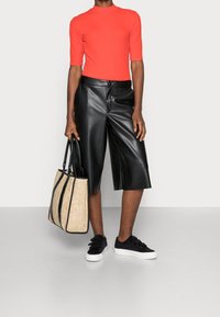 Röd figurpassande skjorta med korta ärmar, svarta faux läder culotter, svarta sneakers och en strukturerad beige toteväska med svarta accenter.