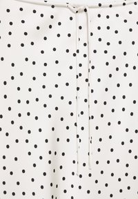 Tissu blanc avec un motif à pois noirs et un fin cordon blanc noué en haut au centre.