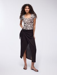 Top fitted con stampa zebra marrone e bianca con maniche corte, abbinato a una lunga gonna nera avvolgente con uno spacco laterale. Sandali piatti neri.