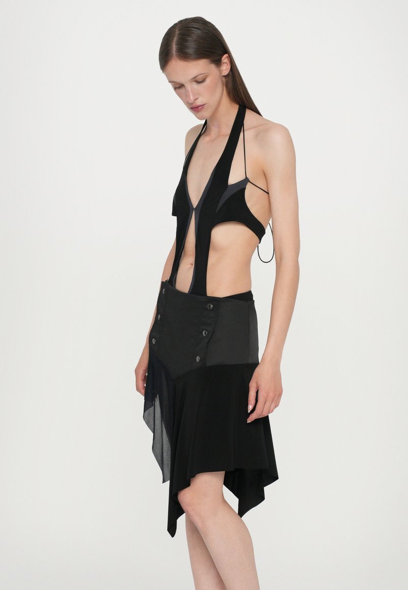 Black, halter-style dress featuring sheer panels and asymmetrical hem. Textured fabric with button accents on the layered skirt.