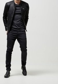 Svart läderjacka med dragkedjefickor, i kombination med en mörk tröja och smala svarta jeans. Avslutad med eleganta svarta ankelkängor.