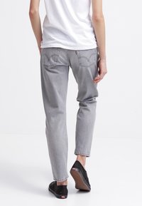 Grå denimjeans med en avslappnad passform, med bakfickor med sömnadsdetaljer. Bärs med en vit t-shirt och svarta slip-on skor.