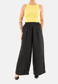 Top sin mangas amarillo acanalado, pantalones de pierna ancha negros con cintura elástica, textura suave y tela fluida. Zapatos negros de punta cerrada.