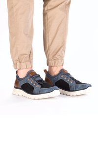 Baskets de sport bleu et noir avec une tige en mesh, des accents en cuir brun, des lacets orange et une semelle blanche texturée.