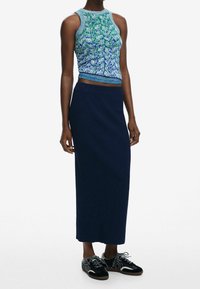 Top corto lavorato a maglia nei toni del blu e verde con motivo a rilievo, abbinato a una lunga gonna blu navy a coste e sneakers nere con texture.