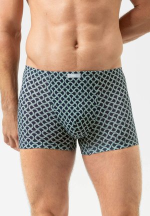 Mannelijke torso met strak zittende boxershorts met een blauw-groen geometrisch golfpatroon op een witte achtergrond.