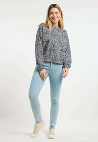 Felpa a fantasia navy con maniche lunghe e pompose, abbinata a jeans skinny azzurri chiari e sneakers beige, su uno sfondo neutro.