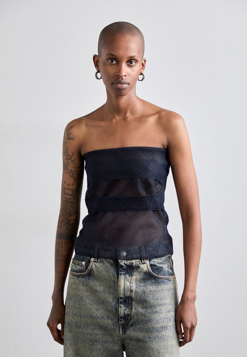 Top senza spalline in rete blu navy con bande orizzontali testurizzate, abbinato a jeans in denim chiaro con vestibilità rilassata e chiusura con bottone anteriore.