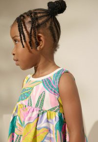 Buntes, ärmelloses Kleid mit einem Blumen- und Blattmuster in Pink, Gelb, Türkis und Grün, aus leichtem Stoff. Seitenansicht eines Kindes.