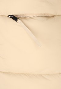 Țesătură bej cu un fermoar parțial deschis, având un mâner negru și o buclă din țesătură bej atașată pentru o prindere ușoară.