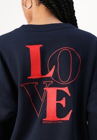 Námornícky sveter s veľkým červeným nápisom "LOVE" na chrbte, s textúrovaným dizajnom. Logo značky "DENIM TOM TAILOR" v malom písme.