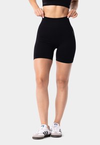 Black high-waisted shorts with a smooth texture, mid-thigh length, and minimal branding detail, paired with white and gray athletic shoes.