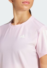 Camiseta atlética de color rosa claro hecha de tela de malla transpirable. Presenta un logotipo blanco en el pecho y tres rayas en los hombros.