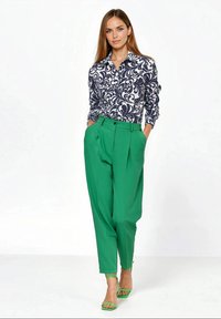 Granatowo-biała koszula zapinana na guziki w wzory, zestawiona z zielonymi spodniami z wysokim stanem i pasującymi zielonymi sandałami. Jasne kolory i wyraźne wzory.