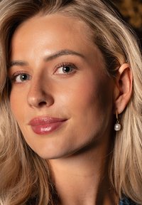 Gold hoop earring with a white pearl accent, featuring a smooth surface and subtle shine. Skin tone is even with natural highlights.