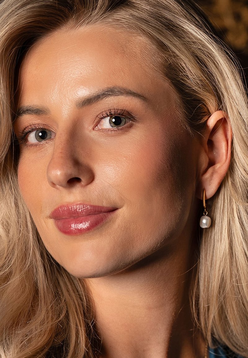 Gold hoop earring with a white pearl accent, featuring a smooth surface and subtle shine. Skin tone is even with natural highlights.