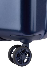 Angolo di una valigia rigida blu navy con una ruota girevole nera caratterizzata da un design a raggi e una superficie liscia.