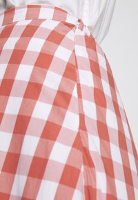 Rot-weißer Vichykaro-Rock mit einem Seitenreißverschluss, der eine klare Textur und einen taillierten Bund aufweist.