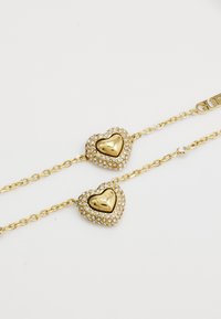 Bracelet en or avec deux breloques en forme de cœur ornées de strass transparents et d'un intérieur en or poli ; les maillons ont une finition brillante.