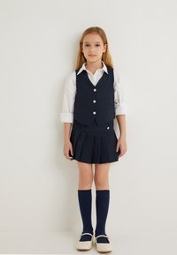 Marine school uniform met een mouwloos vest met knopen, een geplooide rok, een wit shirt, kniekousen en witte schoenen.