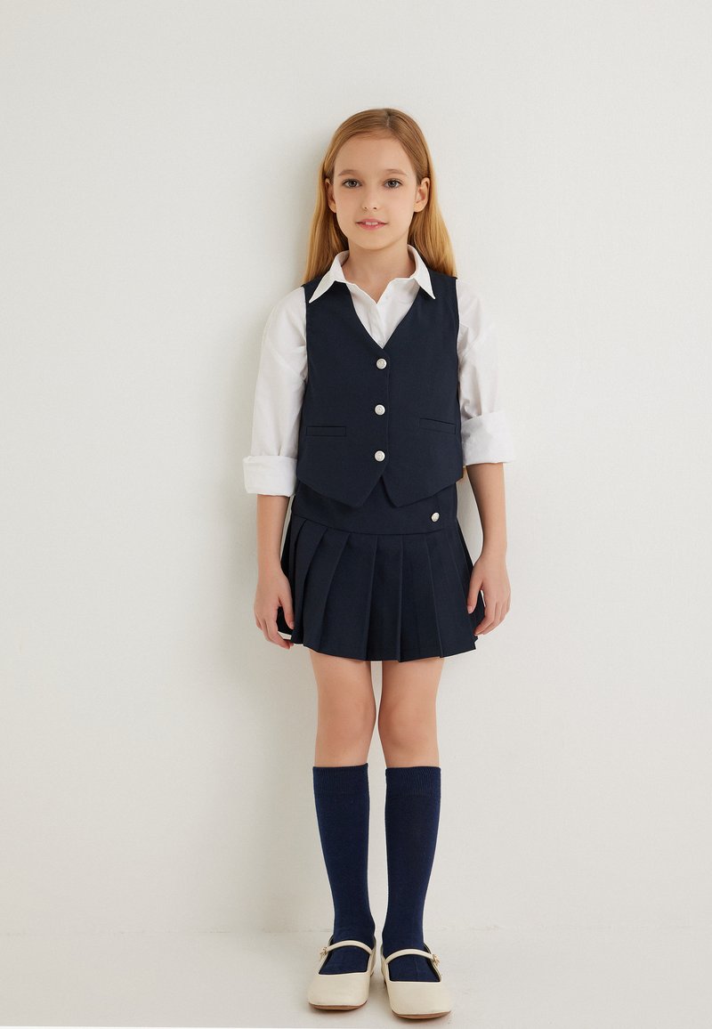 Marine school uniform met een mouwloos vest met knopen, een geplooide rok, een wit shirt, kniekousen en witte schoenen.