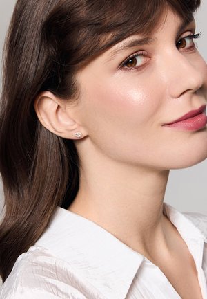 Okrągłe kolczyki z kryształkami, osadzone w metalowej podstawie. Modelka ma na sobie białą koszulę z kołnierzykiem, co wyraźnie eksponuje kolczyki.