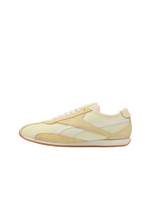 Lage beige en crèmekleurige sneaker met witte veters, suède overlays en een bruine rubberen zool, vanaf de zijkant op een witte achtergrond.