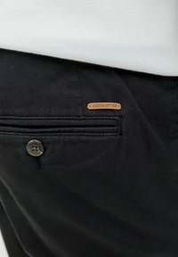 Zwarte broek van een gestructureerde stof, met een knoopsluiting, een achterzak en een klein leren label met de tekst "JACK & JONES."