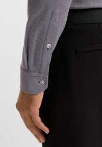 Camicia a maniche lunghe con un motivo testurizzato a piccole pois grigio e bianco, con bottoni argentati ai polsini, abbinata a pantaloni neri.