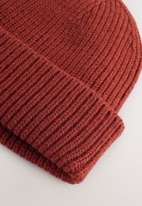 Pleteni zimski šešir u dubokoj hrđavo crvenoj boji, s teksturom rebraste pletenice i preklopljenim rubom. Izrađen od debelog prediva za toplinu i udobnost.