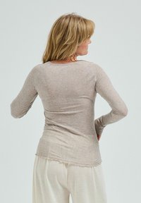 Långärmad, ljusbeige topp med en mjuk textur och rundad fåll, med en subtil lyster och figurnära design, bärs med ljusa byxor.