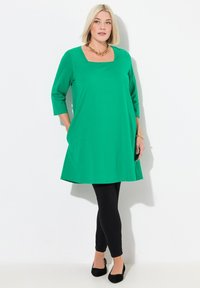 Tunika verde a maniche 3/4 con scollatura quadrata, abbinata a leggings neri e ballerine nere. Presenta un tessuto morbido e una vestibilità rilassata.