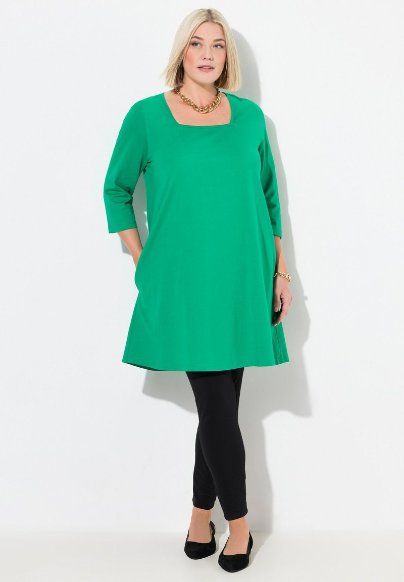 Tunika verde a maniche 3/4 con scollatura quadrata, abbinata a leggings neri e ballerine nere. Presenta un tessuto morbido e una vestibilità rilassata.