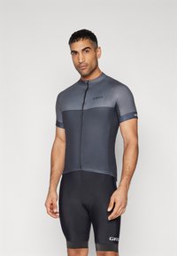 Tricou de ciclism cu mânecă scurtă în gri închis, cu fermoar în față, având o parte superioară texturată și o secțiune inferioară netedă, asortat cu pantaloni scurți negri căptușați.