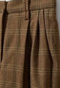 Tissu en laine marron avec un motif à carreaux subtil qui présente des plis et une boucle de ceinture à la taille.