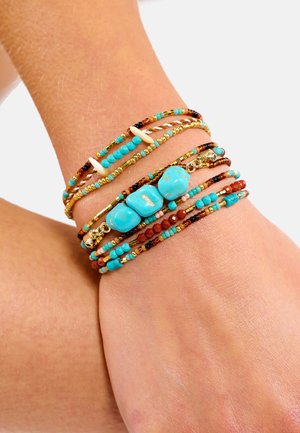 Ensemble de bracelets turquoise et marron avec accents dorés. Plusieurs rangées présentant un mélange de perles petites et plus grandes de formes variées.