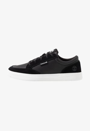 Zapatilla negra de corte bajo con suela blanca, diseño con cordones, logo de Timberland en el lateral y el talón, paneles superiores de piel lisa y ante.