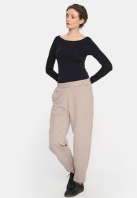 Czarny długi rękaw bluzka z szerokim dekoltem zestawiona z luźnymi, jasnobeżowymi spodniami z bocznymi kieszeniami i elastycznym paskiem w talii. Czarne trampki.