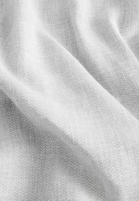 Tissu texturé, gris clair, avec une apparence douce et tissée. La surface présente un motif subtil, avec des fibres visibles indiquant une structure textile.