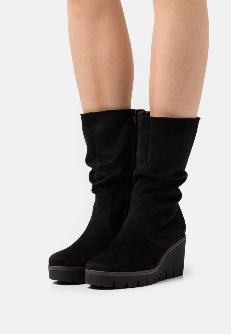 Bottes compensées en daim noir mi-mollet avec fermeture éclair latérale, portées sur des jambes nues, présentant une semelle plateforme rainurée et un design de tige ample.