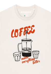 Cremefarbenes T-Shirt mit einem schwarzen und roten Grafikdesign einer French Press und zwei Gläsern. Der Text lautet: "KAFFEE macht alles besser."