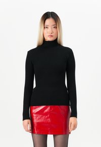 Μαύρο ριμπ ζιβάγκο πουλόβερ με μακριά μανίκια, συνδυασμένο με μια γυαλιστερή κόκκινη δερμάτινη μίνι φούστα. Λείος υφασμάτινος σχεδιασμός και εφαρμοστό κόψιμο.