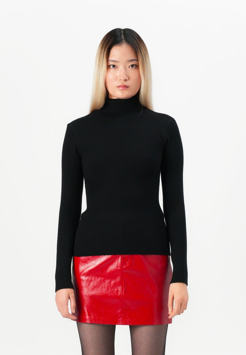 Μαύρο ριμπ ζιβάγκο πουλόβερ με μακριά μανίκια, συνδυασμένο με μια γυαλιστερή κόκκινη δερμάτινη μίνι φούστα. Λείος υφασμάτινος σχεδιασμός και εφαρμοστό κόψιμο.