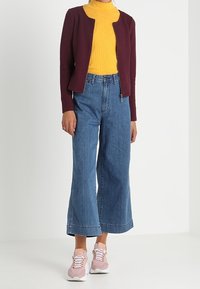 Maroontexturerad jacka, gul ribbad rullkrage, vida blå jeans och ljusrosa sneakers med vita sulor och snören.