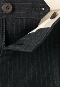 Tessuto nero a righe con una texture morbida presenta una chiusura con zip e bottone. Include dettagli aggiuntivi in tessuto e bottone.