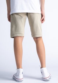 Beige shorts van katoen, met een eenvoudig ontwerp en gestikte zoom, gecombineerd met witte hoge sneakers, tegen een lichte achtergrond.